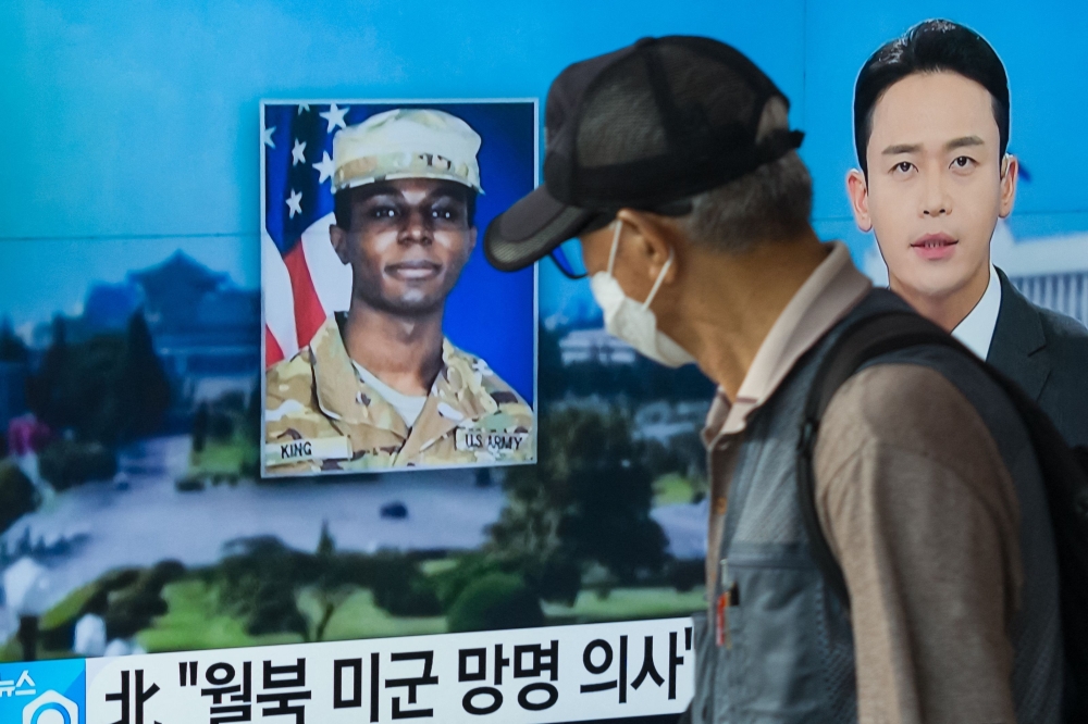 (Files) In this photo taken in Seoul on August 16, 2023, a man walks past a television showing a news broadcast featuring a photo of US soldier Travis King (C). (Photo by Anthony Wallace / AFP)