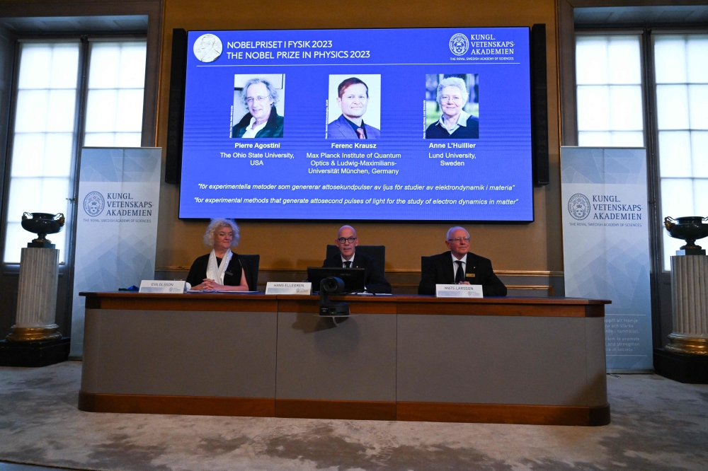 (L-R) US-based physicist Pierre Agostini, Hungarian-Austrian physicist Ferenc Krausz and French physicist Anne L' Huillier appear on the screen as member of the Royal Swedish Academy of Sciences Chair of the Nobel Committee for Physics Eva Olsson, Secretary General of the Royal Swedish Academy of Sciences and Member of the Nobel Committee For Physics speak during the announcement on October 3, 2023. (Photo by Jonathan Nackstrand / AFP)