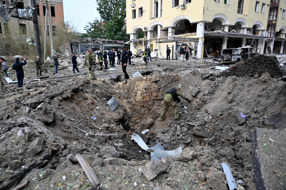 An expert examines a crater after a Russian strike to the centre of the Ukrainian city of Kharkiv on October 6, 2023, amid Russian invasion in Ukraine. (Photo by Sergey Bobok / AFP)