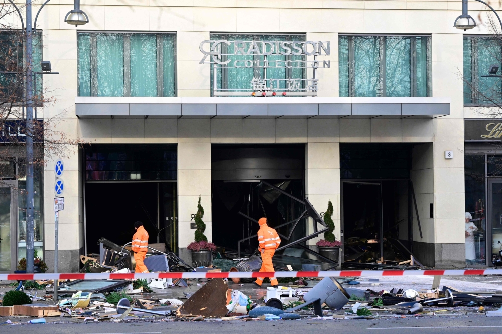 (Files) Workers of the city cleaning department walk past debris covering the street in front of the Radisson Blu hotel after a huge aquarium burst on December 16, 2022 in Berlin. (Photo by John MacDougall / AFP)