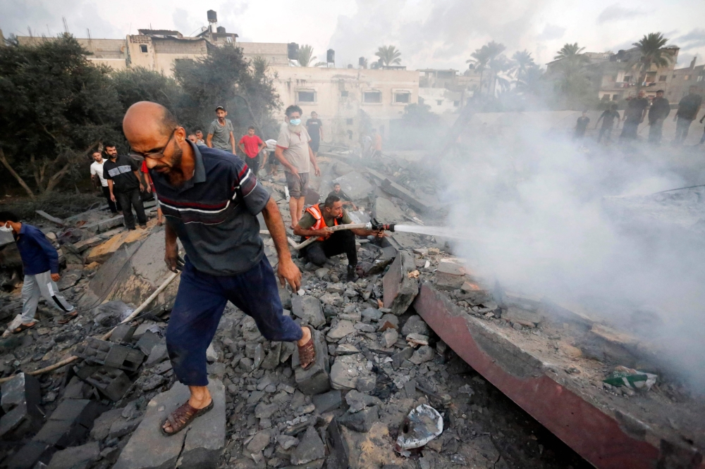 A Palestinian civil defence operator sprays water to douse the area of a building destroyed following an Israeli attack on the town of Deir Al-Balah, in the central Gaza Strip, on October 15, 2023. (Photo by Mohammed Faeq / AFP)