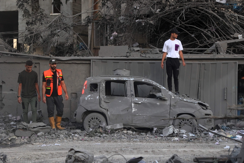 A rescuer and people stand near a burnt car following an Israeli strike in Rafah in the southern Gaza Strip, on October 15, 2023. (Photo by Said Khatib / AFP)