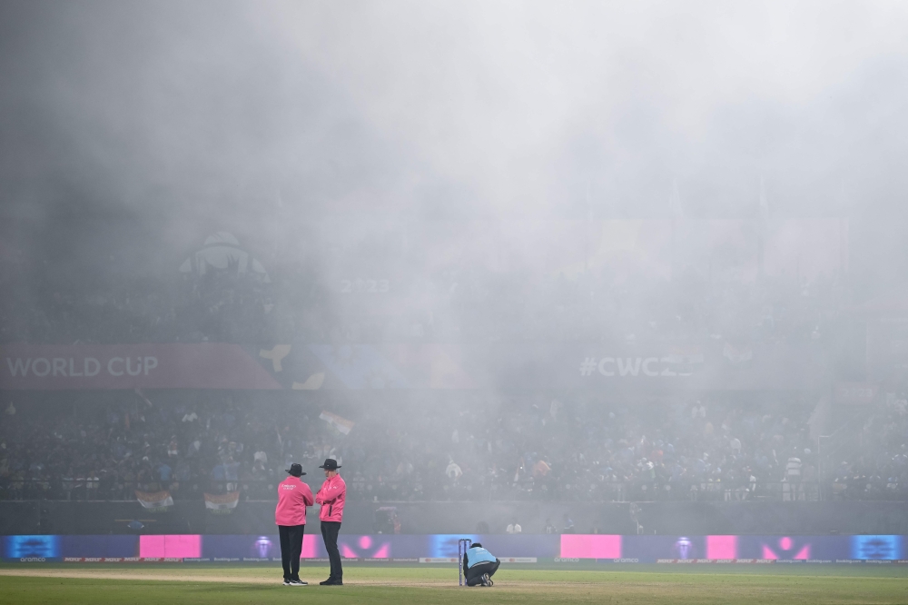 Field umpires stand on the pitch as fog hovers over the field during the 2023 ICC Men's Cricket World Cup one-day international (ODI) match between India and New Zealand at the Himachal Pradesh Cricket Association Stadium in Dharamsala on October 22, 2023. (Photo by Money SHARMA / AFP)