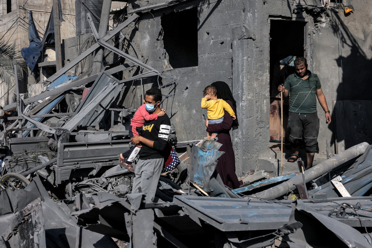 A man and woman walk carrying children past the rubble of a building hit by Israeli bombardment in Rafah in the southern Gaza Strip on October 31, 2023. (Photo by MOHAMMED ABED / AFP)