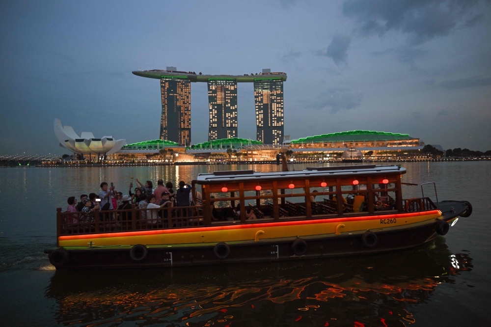 A boat crosses the Marina Bay Sands hotel resort (background), seen lit up in green to celebrate the Earthshot Prize and United for Wildlife, in Singapore on November 6, 2023. (Photo by Mohd Rasfan / AFP)