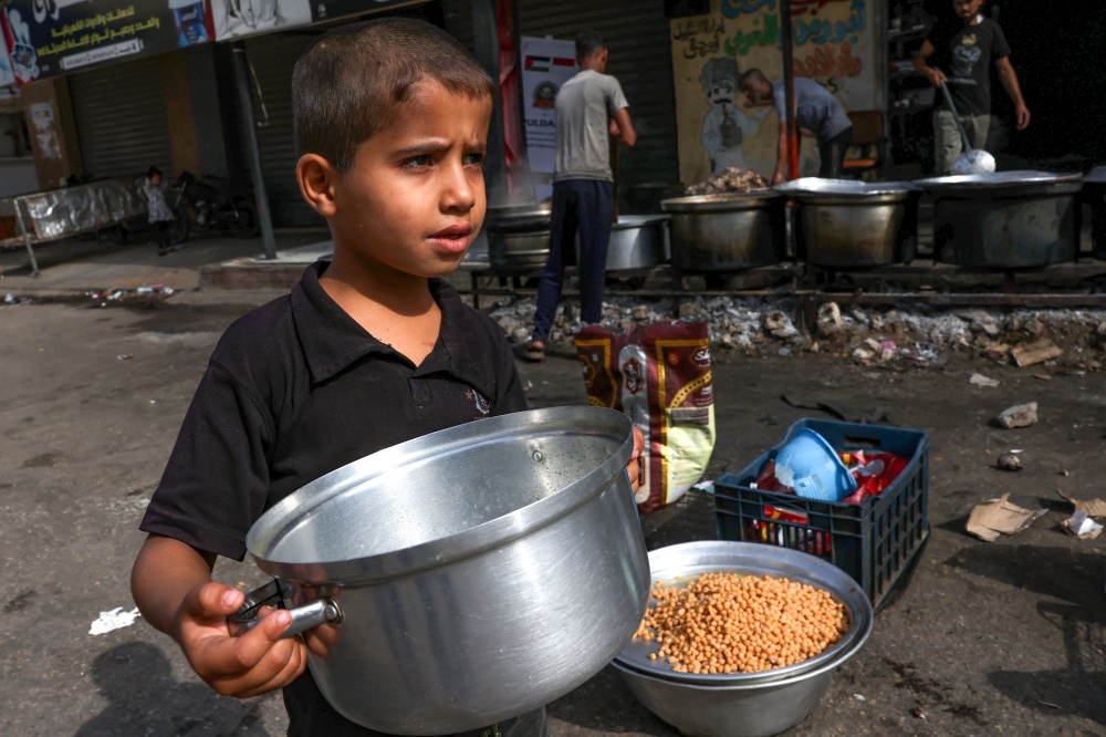 A child carries a pot as Palestinians cook in a street in Rafah in the southern Gaza Strip, on November 8, 2023. Photo by MOHAMMED ABED / AFP