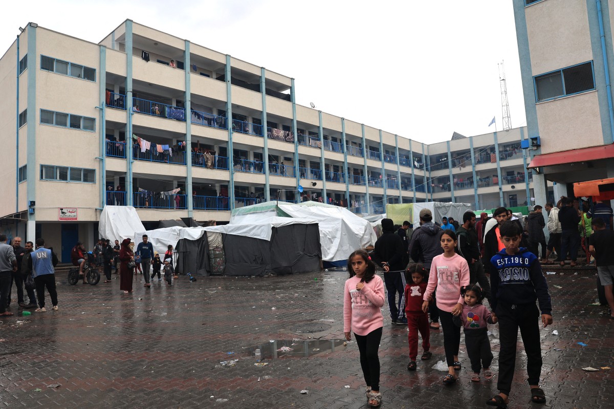 Internally displaced Palestinian children living in a school run by the UN agency for Palestinian refugees (UNRWA), walks across a wet courtyard following overnight rainstorms in Rafah in the southern Gaza Strip on November 15, 2023. Photo by SAID KHATIB / AFP