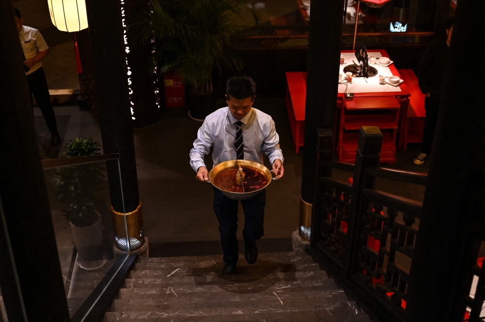 This photo taken on October 21, 2023 shows a restaurant employee taking away a pot of oily broth, which will be recycled, at an eatery in Chengdu, China's southwest Sichuan province. Photo by Hector RETAMAL / AFP