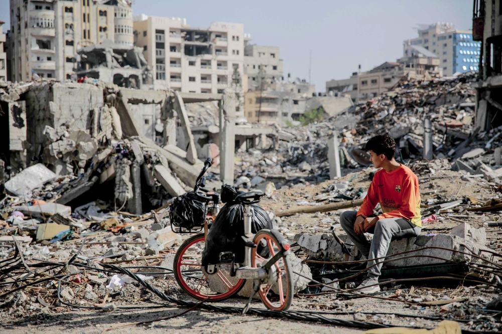 A Palestinian youth sits next to his bicycle amid the rubble of destroyed buildings in Gaza City on the northern Gaza strip on November 24, 2023. (Photo by AFP)