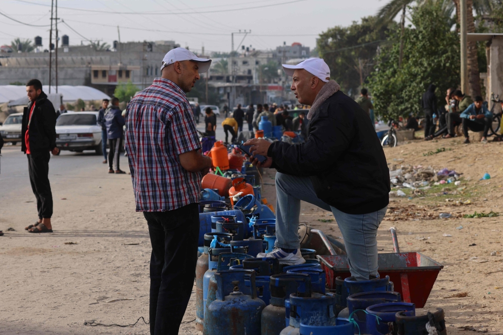 People wait near empty gas canisters to be filled with cooking gas from a tank that entered the Palestinian enclave on November 25, 2023. (Photo by Said Khatib / AFP)
