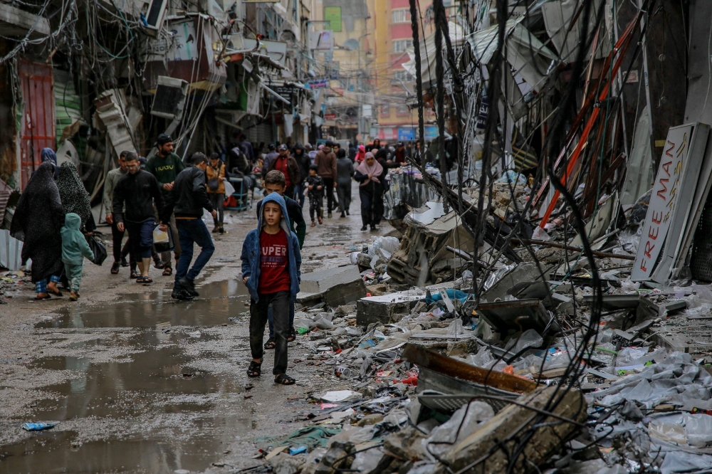 Palestinians walk amid debris of buildings hit in Israeli strikes, near Al-Zawiya market in Gaza City on November 27, 2023. (Photo by Omar El-Qattaa / AFP)
