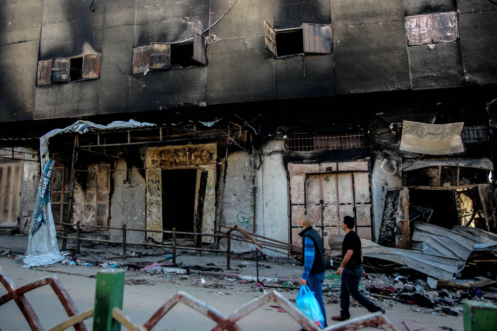 People walk past the Gaza municipality building in Gaza City on November 30, 2023. (Photo by Omar El-Qattaa / AFP)