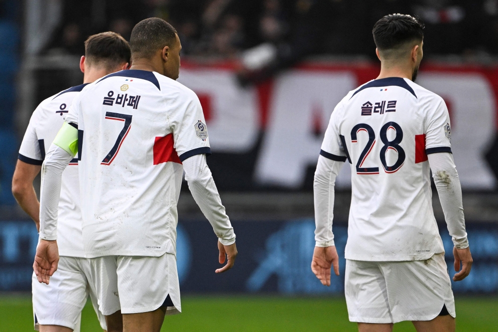 Paris Saint-Germain's French forward #07 Kylian Mbappe (C) and Paris Saint-Germain's Spanish midfielder #28 Carlos Soler stand as they are wearing a jersey flocked in corean, during the French L1 football match between Le Havre AC and Paris Saint-Germain (PSG) at The Stade Oceane in Le Havre, north-western France, on December 3, 2023. (Photo by DAMIEN MEYER / AFP)
