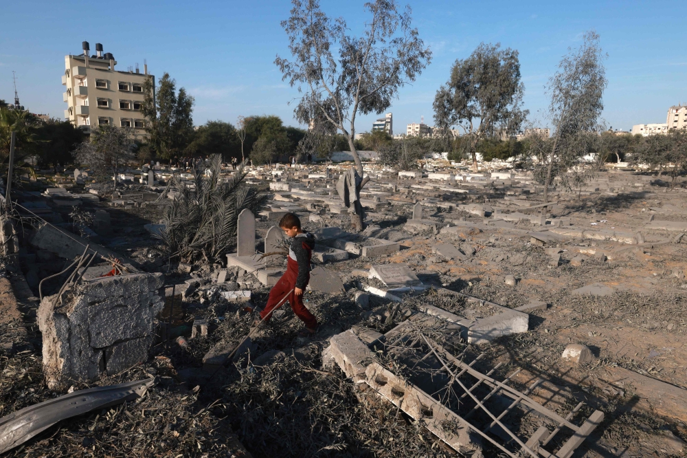 A Palestinian boy collects wood near a cemetery damaged following Israeli air strikes in Rafah in the southern Gaza Strip early on December 4, 2023. (Photo by Mohammed Abed / AFP)
 