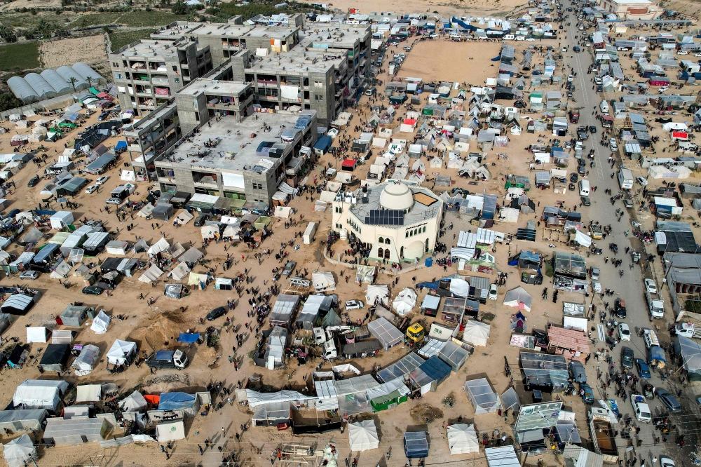 This aerial view taken on December 9, 2023 shows the makeshift tent camps housing Palestinians displaced by intense Israeli bombardment on the Gaza Strip seeking refuge in open areas around the Raed al-Attar Mosque in Rafah in the southern Gaza Strip near the Egyptian border. Photo by SAID KHATIB / AFP