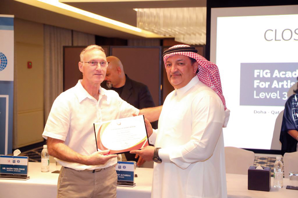 Qatar Gymnastics Federation President Ali Al Hitmi (right) presents a certificate to a participant.
