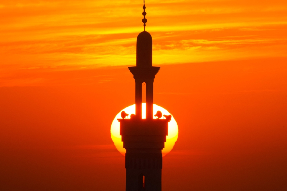 A picture taken from Rafah in the southern Gaza Strip on December 10, 2023, shows the minaret of a mosque silhouetted against the setting sun amid. (Photo by Mahmud Hams / AFP)