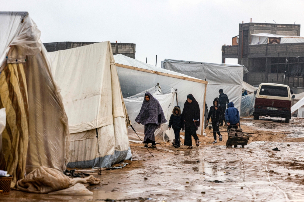 Palestinians walk under the rain at a camp for displaced people in Rafah, in the southern Gaza Strip where most civilians have taken refuge, on December 13, 2023. (Photo by Mahmud Hams / AFP)