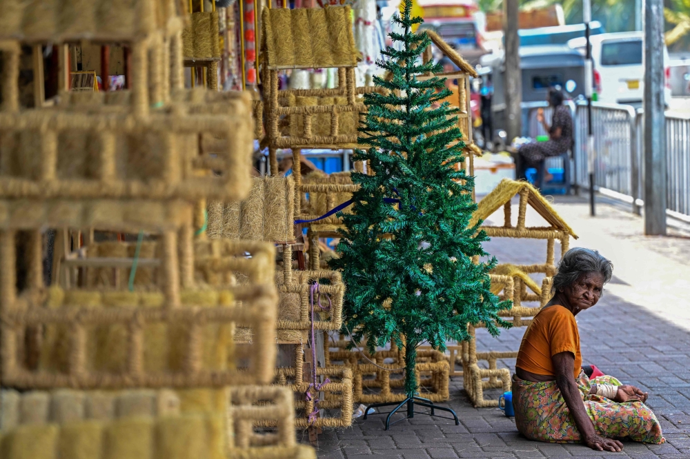 A beggar sits beside a Christmas tree along a road in Colombo on December 20, 2023. (Photo by Ishara S. KODIKARA / AFP)