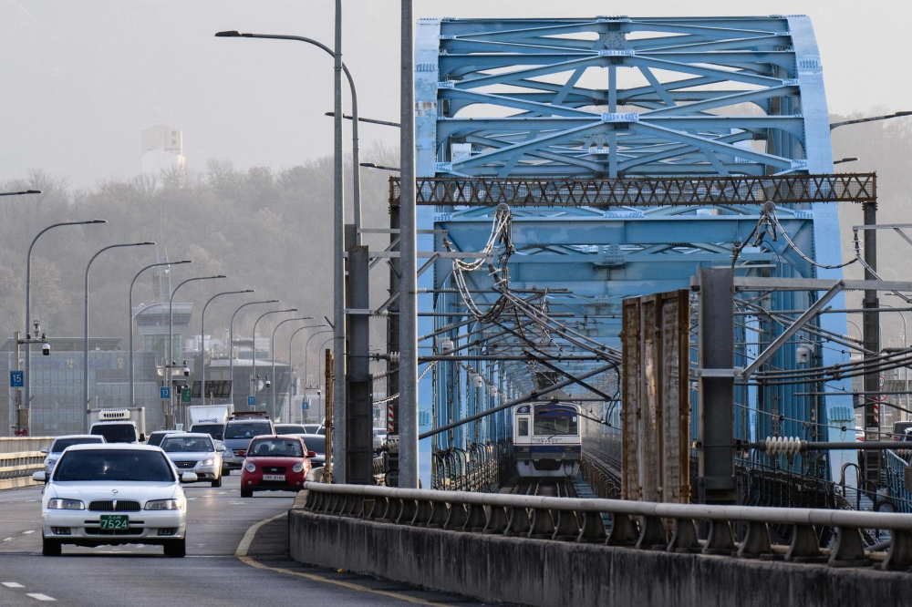 A Seoul Subway Line 4 metro train drives next to cars over the Dongjak Bridge, which runs across the Han River, in Seoul on December 7, 2023. (Photo by Anthony WALLACE / AFP)

