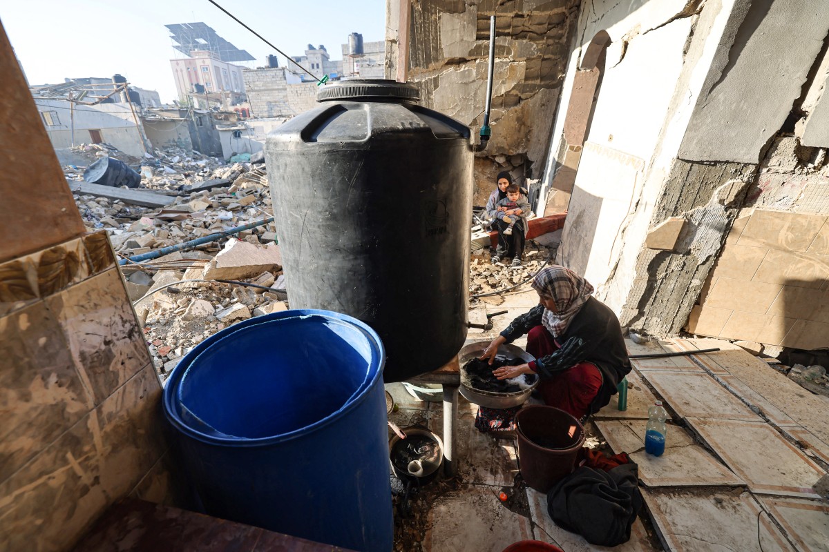 A woman washes clothes in her destroyed house in Rafah in the southern Gaza Strip on December 18, 2023. (Photo by Mohammed Abed / AFP)
