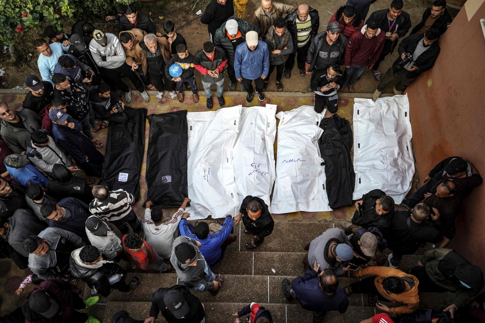 People stand over the shrouded bodies of loved ones killed during Israeli bombardment at Nasser Hospital in Khan Yunis on the southern Gaza Strip on December 27, 2023. Photo by AFP