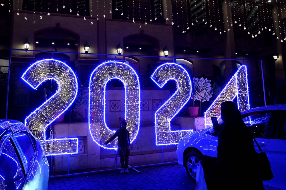 A woman takes photo of her child in front of a 2024 illuminated sign displayed in Islamabad on December 29, 2023. (Photo by Aamir Qureshi / AFP)