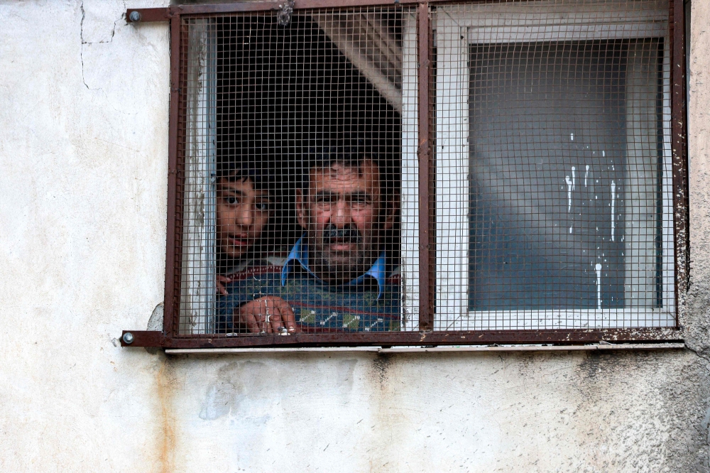 A man and a boy look out the window of a building at the scene where Palestinians were shot in the town of Azzun, east of Qalqilya in the occupied West Bank, on January 2, 2024. (Photo by Jaafar Ashtiyeh / AFP)