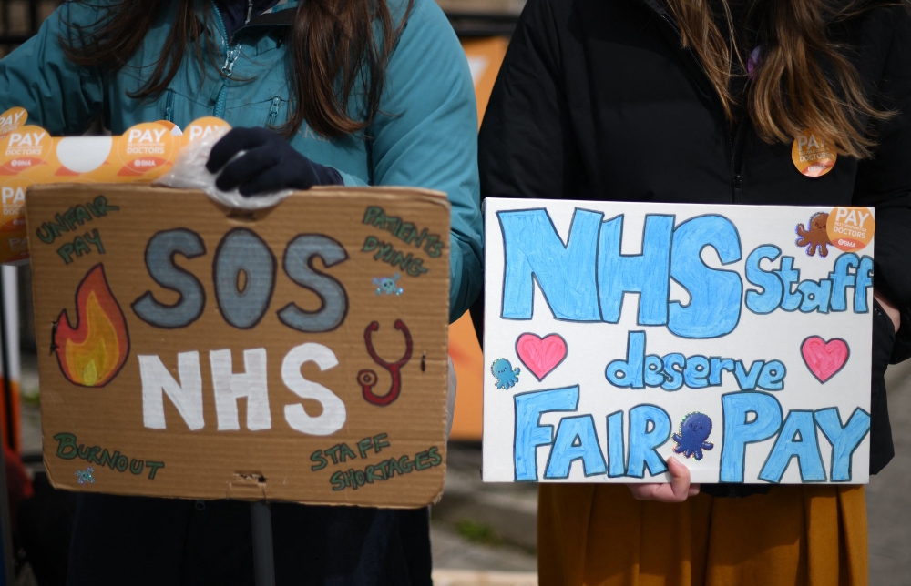 People hold placards calling for fairer pay on a picket line outside Great Ormond Street Children's Hospital in London on April 12, 2023, on the second day of a strike by NHS junior doctors -- physicians who are not senior specialists but who may still years of experience. Photo by Daniel LEAL / AFP