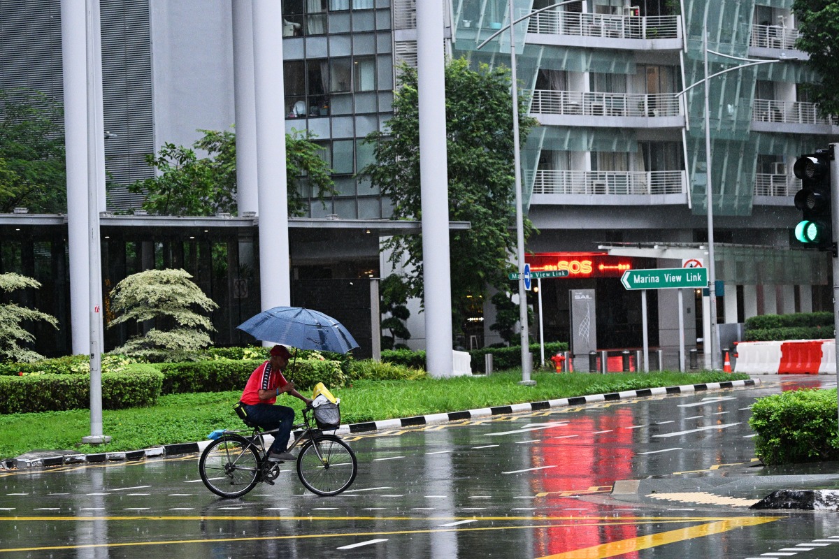  A man holding an umbrella rides in rain in Singapore, Jan. 4, 2024. (Photo by Then Chih Wey/Xinhua)