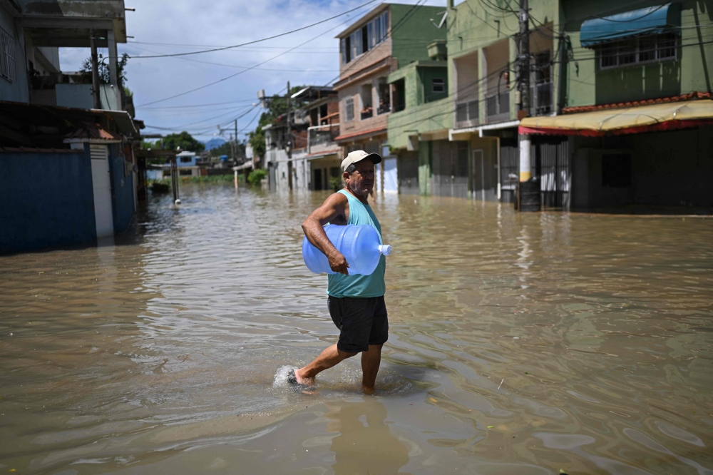 A man carrying a water bottle wades through the water in a flooded area of the Lote XV community in Duque de Caxias, Rio de Janeiro State, Brazil, on January 15, 2024. (Photo by Mauro PIMENTEL / AFP)
