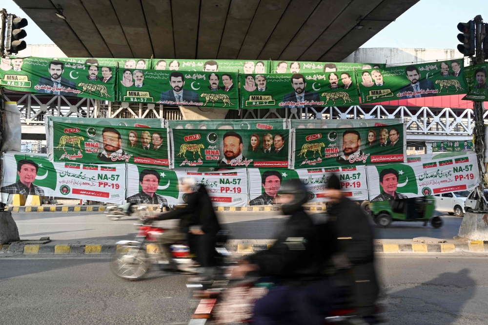 Commuters ride past banners of Pakistan's political parties displayed along a street in Rawalpindi on January 15, 2024. (Photo by Aamir Qureshi / AFP)