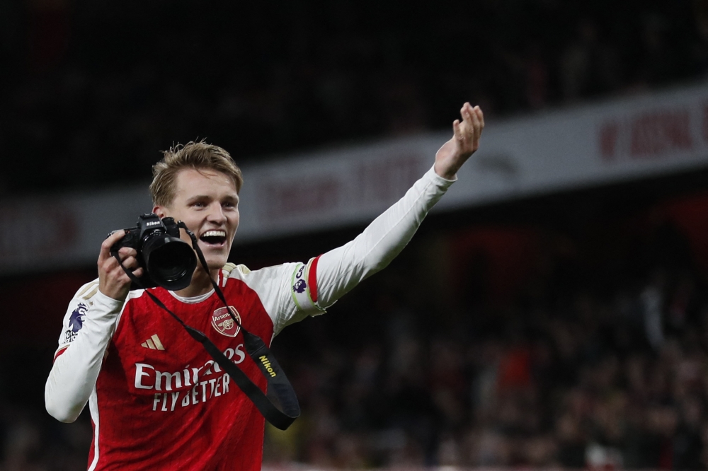 Arsenal's Norwegian midfielder #08 Martin Odegaard picks up a camera and takes pictures as he celebrates at the end of the English Premier League football match between Arsenal and Liverpool at the Emirates Stadium in London on February 4, 2024. (Photo by Ian Kington / IKIMAGES / AFP)