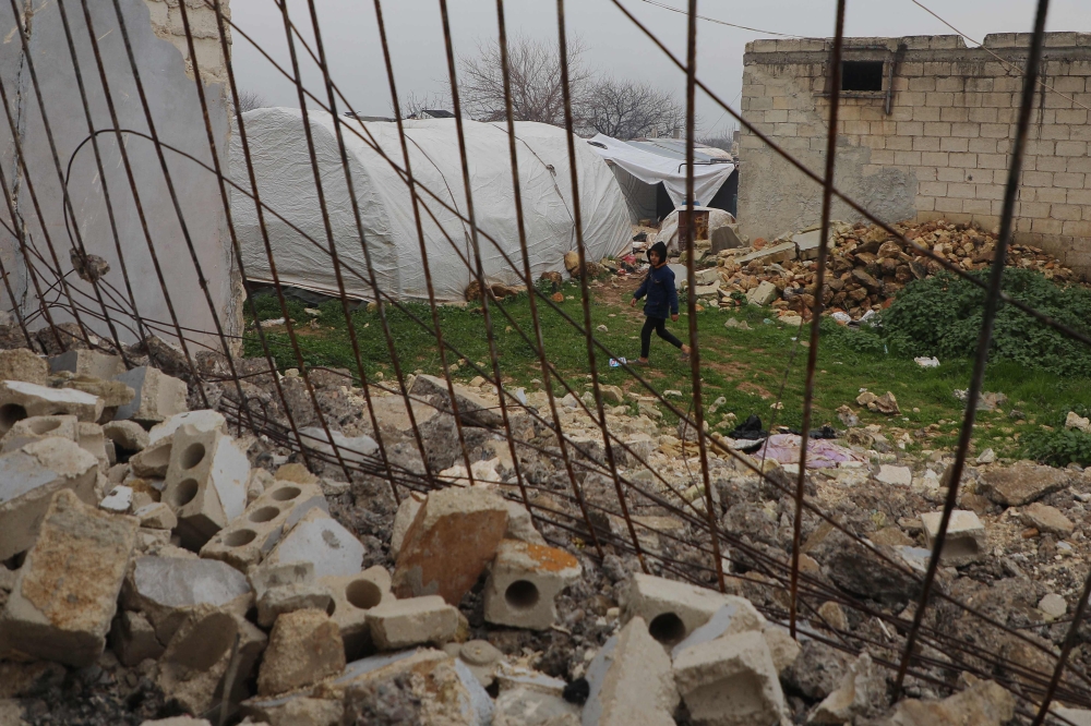 A child walks past a destroyed house at a camp for quake-displaced Syrians in Jindayris town in the northwest of Aleppo province on February 3, 2024. (Photo by Aaref Watad / AFP)