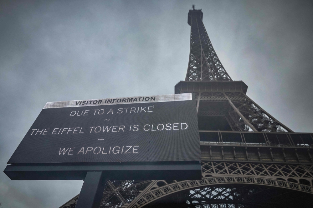 This photograph taken on February 19, 2024, in Paris, shows a board informing visitors that the Eiffel Tower, viewed in the background, is closed as staff go on strike, over the financial management of the monument by the city, closing the monument to the public during the second week of the French school holidays. Photo by Kiran Ridley / AFP