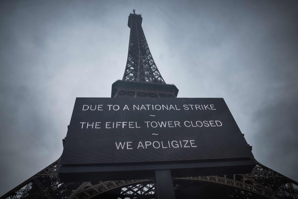 This photograph taken on February 19, 2024, in central Paris, shows a board informing visitors that the Eiffel Tower, viewed in the background, is closed as staff go on strike, over the financial management of the monument by the city, closing the monument to the public during the second week of the French school holidays. (Photo by Kiran RIDLEY / AFP)
