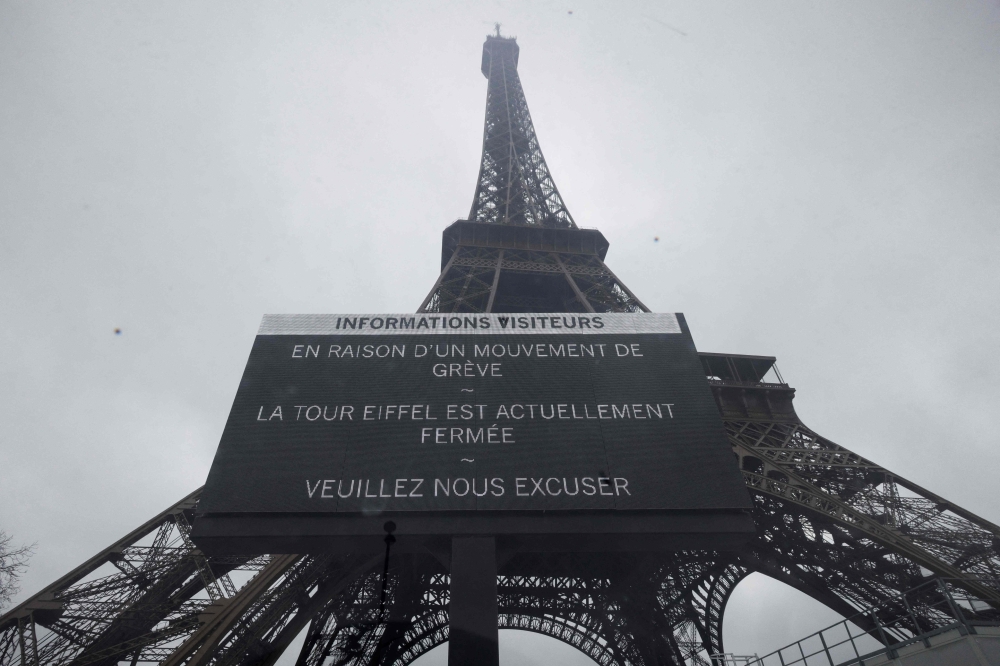 This photograph shows a board informing visitors that the Eiffel Tower, viewed in the background, is closed, during a strike of the Eiffel Tower's staff, over the financial management of the monument by the city, closing the monument to the public during the second week of the French school holidays, in Paris on February 20, 2024. Photo by GEOFFROY VAN DER HASSELT / AFP