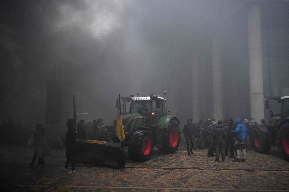 Farmers gather near a tractor as smoke rises during a protest called by the farmers' organizations 