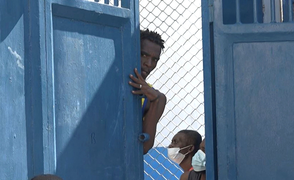 This screen grab taken from AFPTV shows a person looking out from behind a door near the main prison of Port-au-Prince, Haiti, on March 3, 2024, after a breakout by several thousand inmates. (Photo by Luckenson JEAN / AFPTV / AFP)
