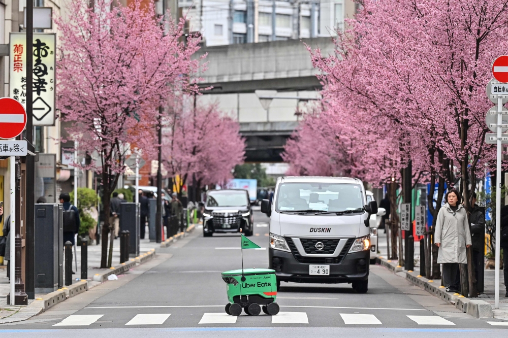 An unmanned robot (C) navigates across a street during a demonstration of a robot delivery service by Uber Eats Japan, Mitsubishi Electric and robot developer Cartken in downtown Tokyo on March 5, 2024. (Photo by Richard A. Brooks / AFP)