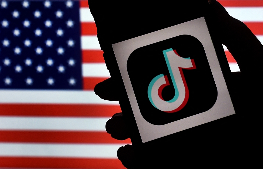 In this photo illustration, the social media application logo, TikTok is displayed on the screen of an iPhone on an American flag background on August 3, 2020 in Arlington, Virginia. Photo by Olivier DOULIERY / AFP
