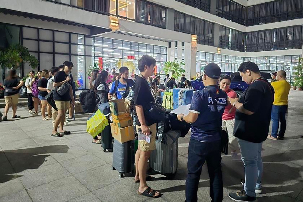 This undated handout photograph received from Philippines' Presidential Anti-Organized Crime Commission (PAOCC) on March 14, 2024 shows a police officer (front, center) talking to foreign nationals after a raid in a 10-hectare (25-acre) complex of buildings in Bamban town of Tarlac province, north of Manila. Hundreds of people forced to work in an online scam centre in the Philippines were rescued in a pre-dawn raid on March 14 that also saw eight suspects arrested, according to police. Police found 432 Chinese nationals, 371 Filipinos, 57 Vietnamese, eight Malaysians, three Taiwanese, two Indonesians and two Rwandans at the site. (Photo by Philippines' Presidential Anti-Organized Crime Commission (PAOCC) / AFP) 