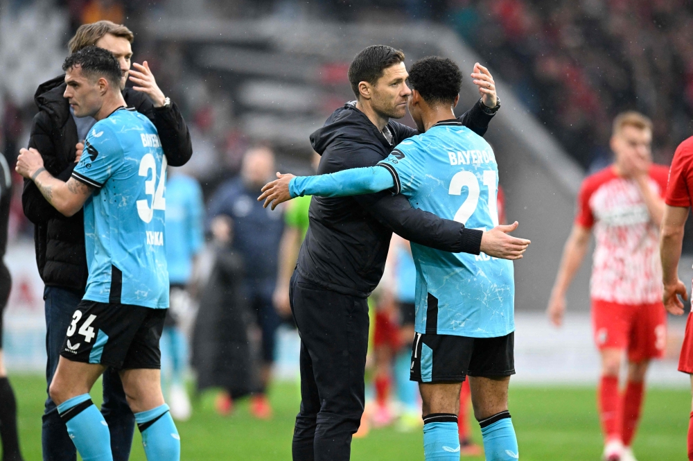 Bayer Leverkusen's Spanish head coach Xabi Alonso (2nd L) embraces Bayer Leverkusen's French forward #21 Amine Adli (R) after the German first division Bundesliga football match SC Freiburg v Bayer 04 Leverkusen in Freiburg, southwestern Germany on March 17, 2024. (Photo by THOMAS KIENZLE / AFP)