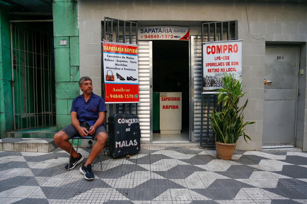 Shoemaker Amilcar Rodriguez, 52, sits outside his store in the central region of Sao Paulo, Brazil on March 20, 2024. (Photo by Miguel SCHINCARIOL / AFP)
