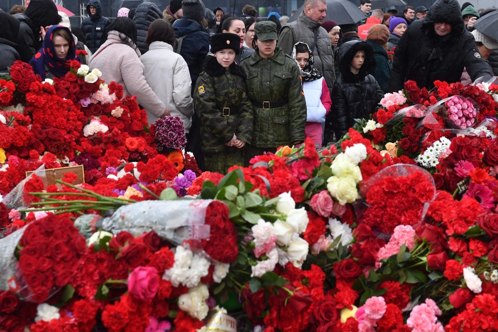 People lay flowers at a makeshift memorial in front of the Crocus City Hall in Krasnogorsk on March 24, 2024, as Russia observes a national day of mourning after a massacre that killed more than 130 people. Photo by Olga MALTSEVA / AFP.