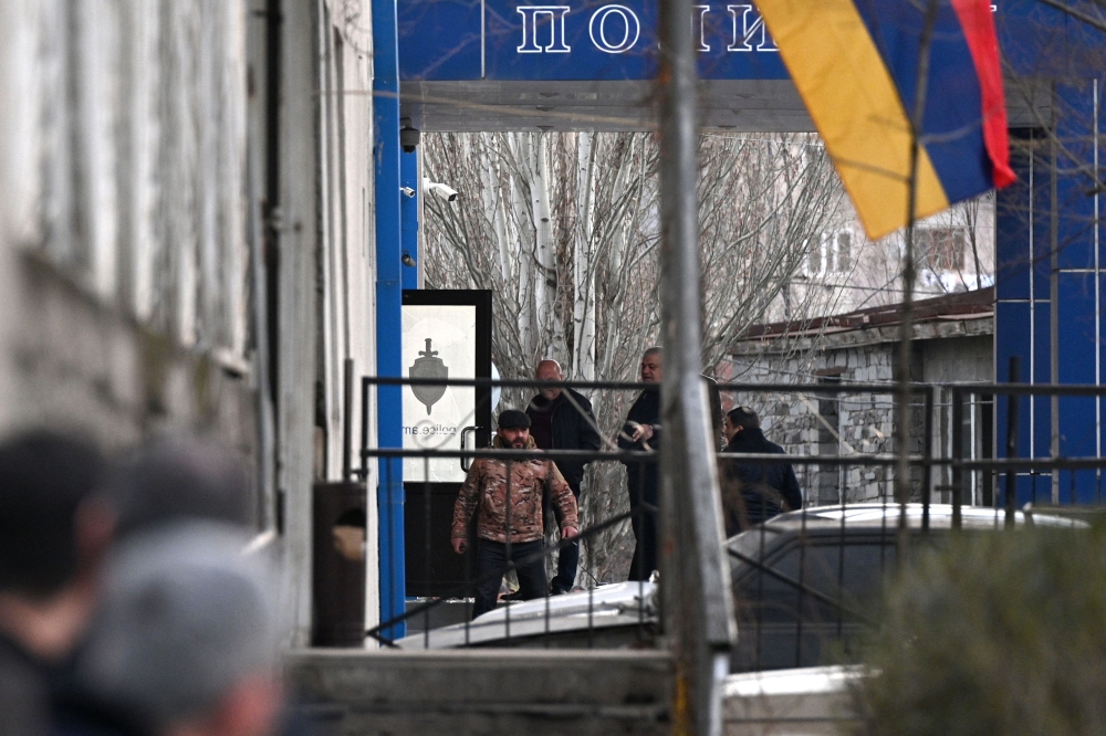 A man (L) holding a hand grenade stands on the porch of a police station in Yerevan on March 24, 2024, during an incident that the Caucasian country's government said was an attempt to seize the building. (Photo by KAREN MINASYAN / AFP)
