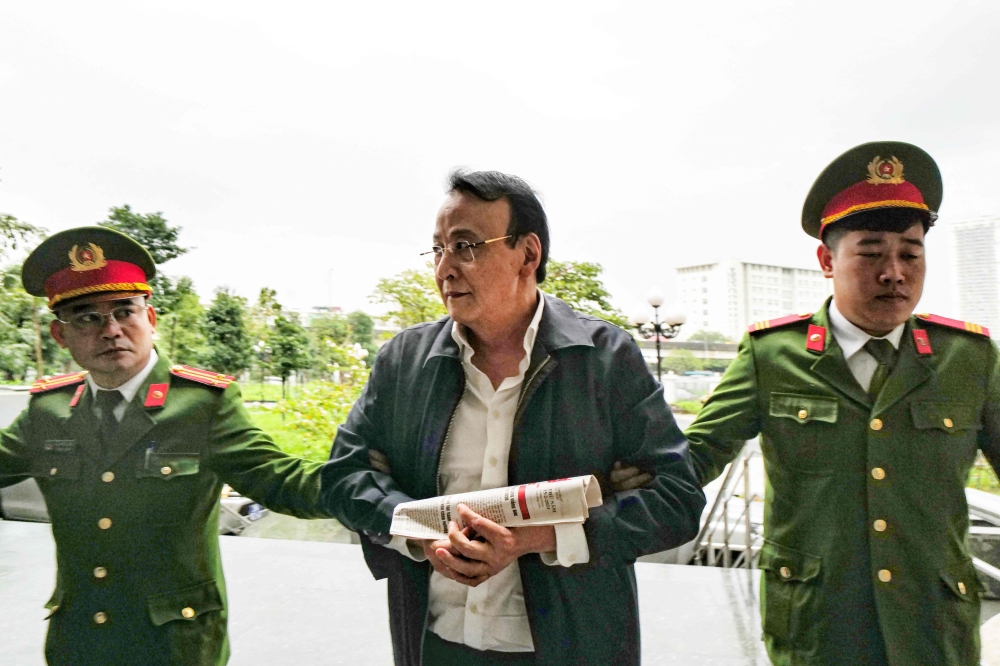 Chairman of Tan Hoang Minh group Do Anh Dung (C) is escorted by police officers to a court for his trial on fraud charges in Hanoi on March 19, 2024. Photo by Anh TUC / AFP