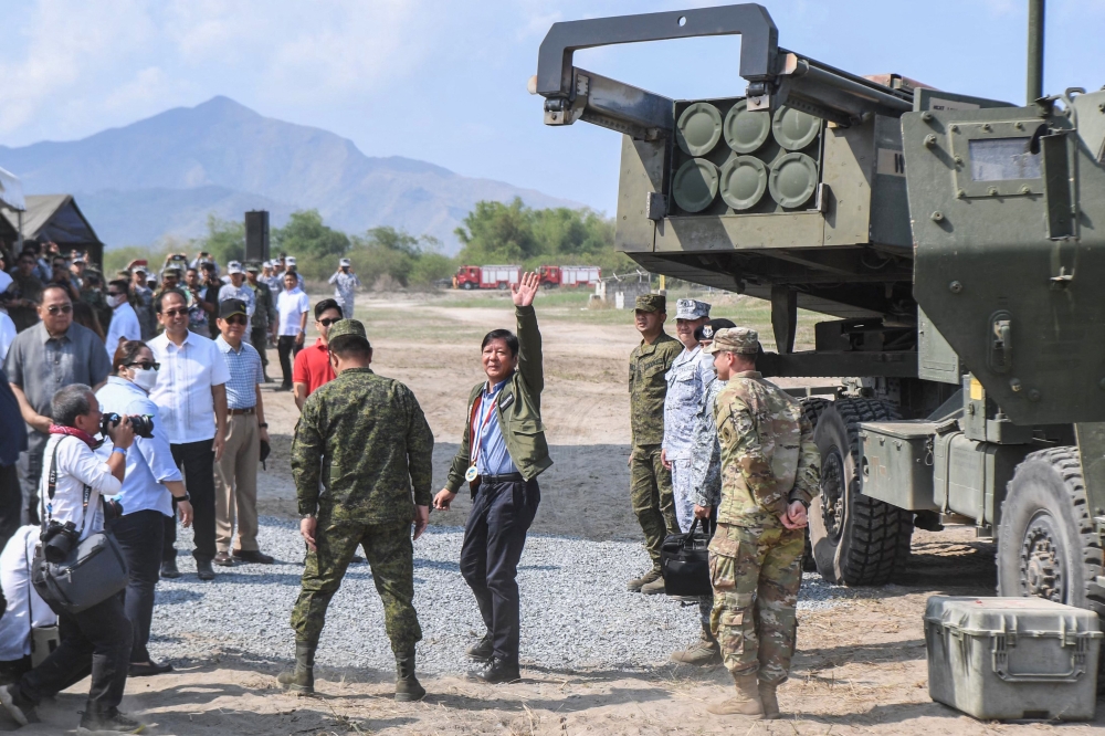  This file photo taken on April 26, 2023 shows Philippine President Ferdinand Marcos (C) waving to photographers after inspecting a high mobility artillery rocket system (HIMARS) before a live fire exercise as part of the US-Philippines Balikatan joint exercise at the naval training base in San Antonio, Zambales province. Photo by Ted ALJIBE / AFP.