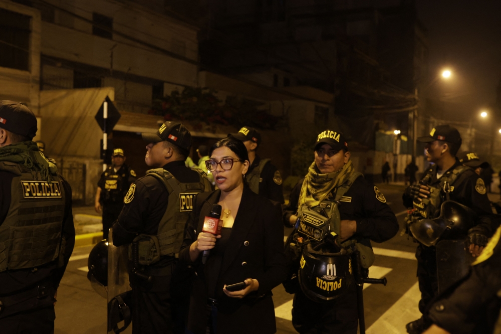 A reporter speaks as police guard outside President Dina Boluarte's house during a raid ordered by the Attorney General's Office as part of a preliminary investigation in Lima on March 30, 2024. (Photo by Juan Carlos CISNEROS / AFP)
