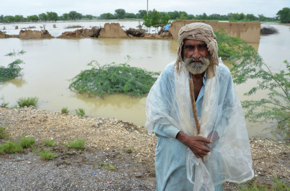 A flood victim covers himself with a plastic sheet to avoid rain, with damaged houses in the background, following rains and floods during the monsoon season in Jafarabd, Pakistan August 26, 2022. REUTERS/Amer Hussain

